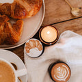 Café setting with croissants, a cup of coffee, and a lit candle on a wooden table.