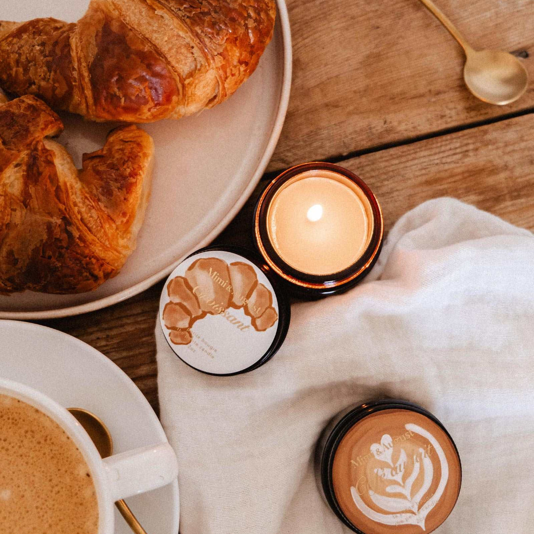 Café setting with croissants, a cup of coffee, and a lit candle on a wooden table.