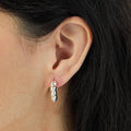 Close-up of an ear wearing a silver hoop earring with dark hair.