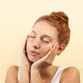 Woman with hands on face against a beige background