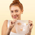 Woman holding a sheet mask against a beige background