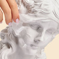 Hand touching a classical sculpture of a woman's head on a beige background