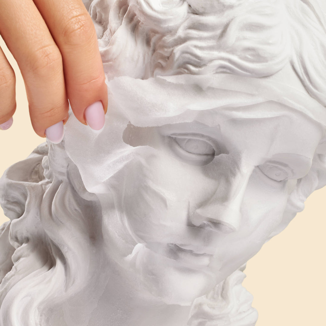 Hand touching a classical sculpture of a woman's head on a beige background