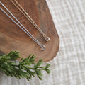 Two silver necklaces with pendants on a wooden surface with a green leaf.