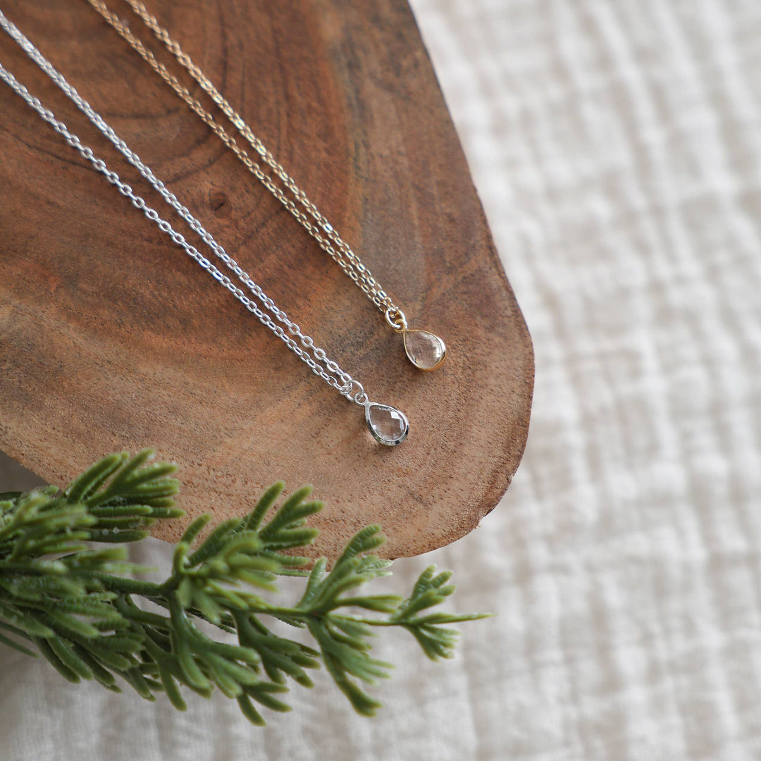 Two silver necklaces with pendants on a wooden surface with a green leaf.