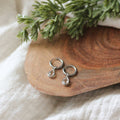 Silver teardrop earrings on a wooden surface with greenery in the background