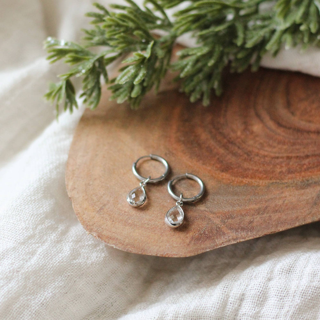 Silver teardrop earrings on a wooden surface with greenery in the background
