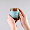 Candle with a blue label held by hands against a gray background