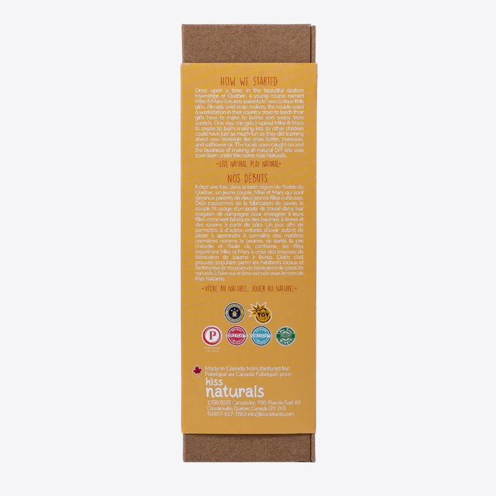 A cardboard box containing a Kiss Naturals Lava Lip Gloss Kit. The box is orange and white with the product name and a colorful illustration of a dragon. It states that the kit is 100% natural, made in Canada, and suitable for ages 6 and up.