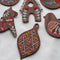 Five embroidered wooden ornaments arranged on a white surface. The ornaments depict a snowflake, a gingerbread house, a Dala horse, a bird, and a geometric design. The ornaments are decorated with colorful embroidery stitches.