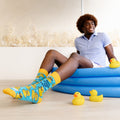 Person sitting on an inflatable pool with rubber duckies and socks featuring duck designs.
