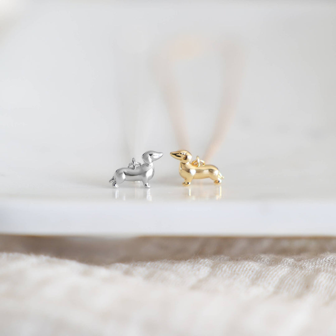 Silver and gold dachshund-shaped earrings on a white surface.