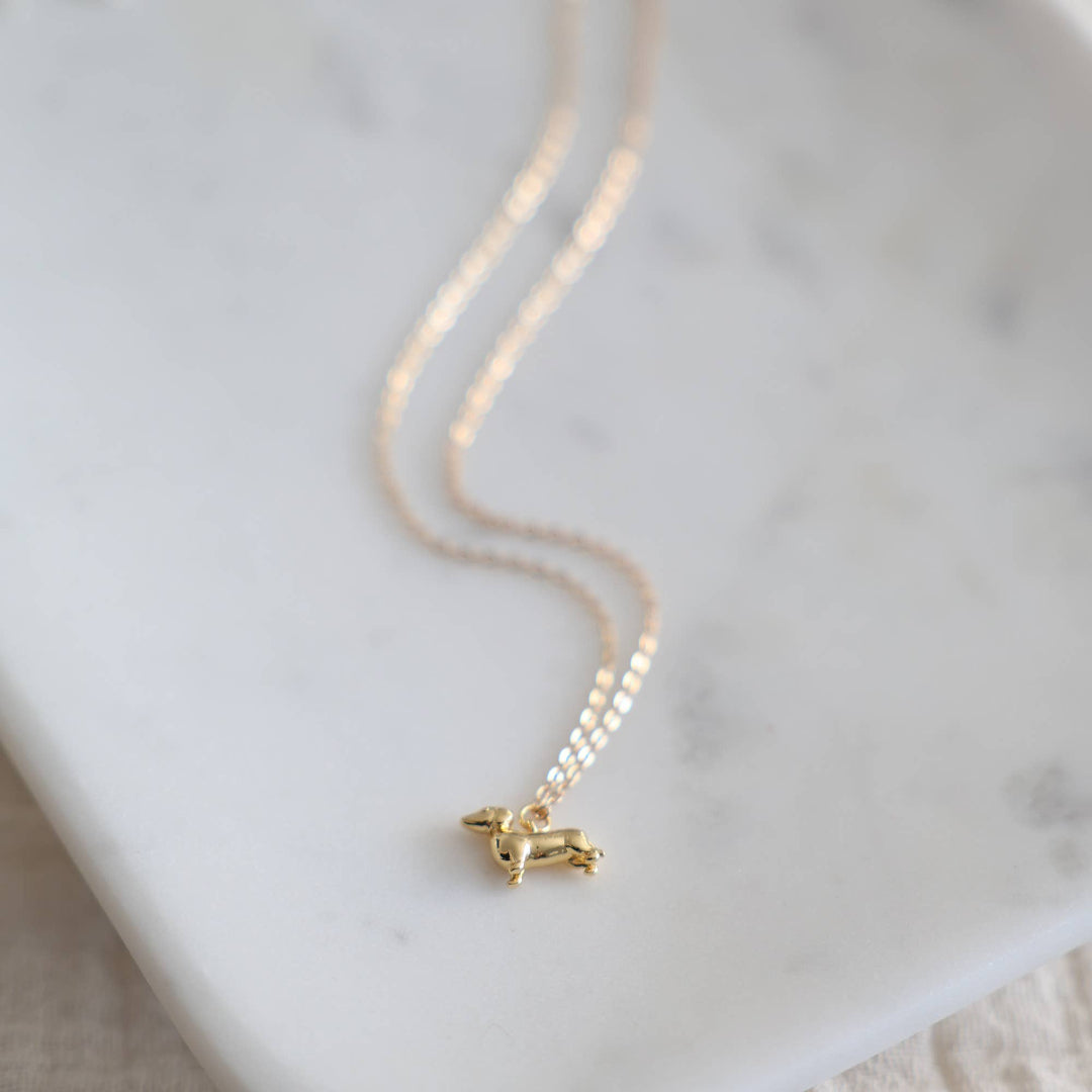 Gold necklace with a small pendant on a marble surface
