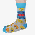 A pair of grey crew socks featuring a "Dad Jokes Loading..." graphic with a progress bar in red and blue, surrounded by various yellow and orange emoji faces. The text "DAD JOKES" is written in blue above the loading bar. The cuff, heel, and toe of the sock are light blue.