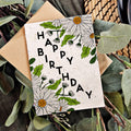 Birthday card with floral design and 'Happy Birthday' text, surrounded by greenery.