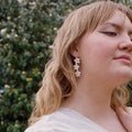 Woman wearing floral earrings with a blurred background of greenery