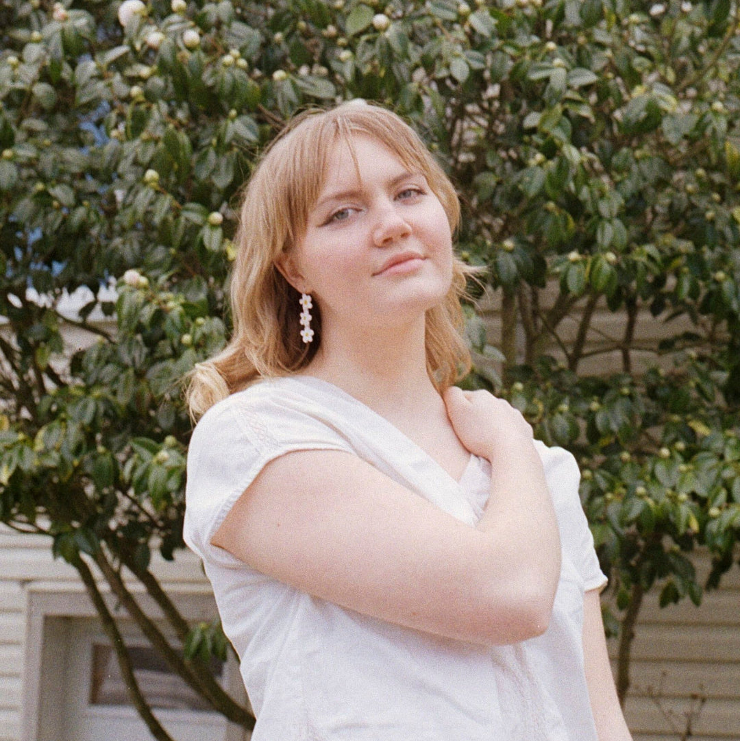 Woman in a white dress standing outdoors with greenery in the background