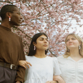Three people standing together with cherry blossom trees in the background