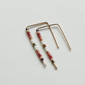 A pair of minimalist U-shaped stud earrings crafted from delicate 14 KT gold wire. Each earring features a short segment of small Japanese glass seed beads in a pattern of red, beige, white, olive green, and brown near the top of the hanging bar.