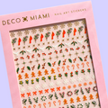 A sheet of Christmas-themed nail art stickers. The sheet is pink and has the brand name "Deco Beauty" printed on it. There's a section titled "Deco the Halls" and instructions on how to apply the stickers. The stickers include various Christmas-themed designs like snowflakes, bells, ornaments, and candy canes.