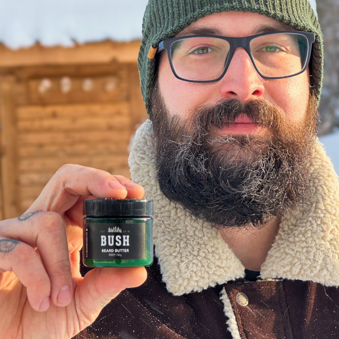 Man holding a jar of 'BUSH Beard Butter' outdoors in winter.