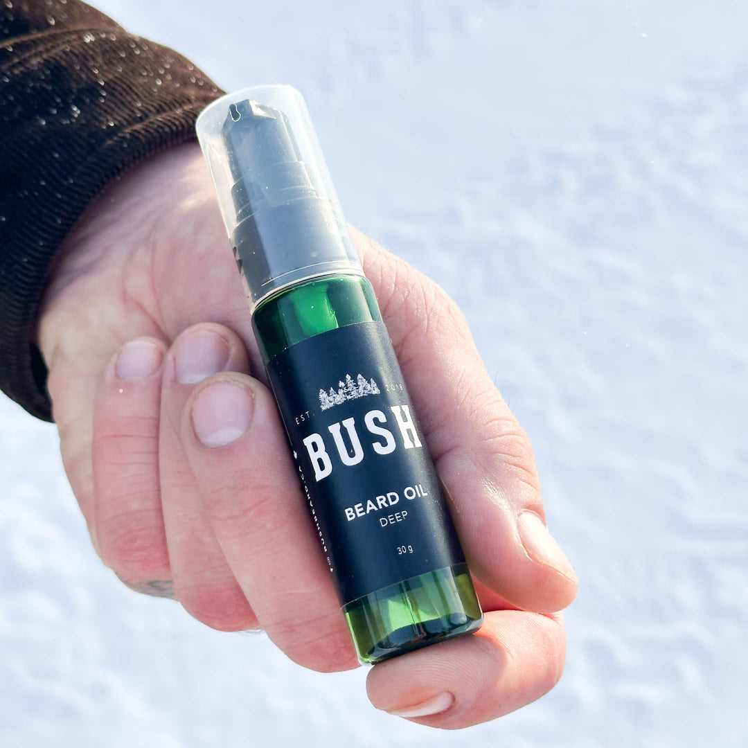 Hand holding a bottle of Bush beard oil against a snowy background