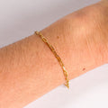 Gold chain bracelet on a wrist with a plain background