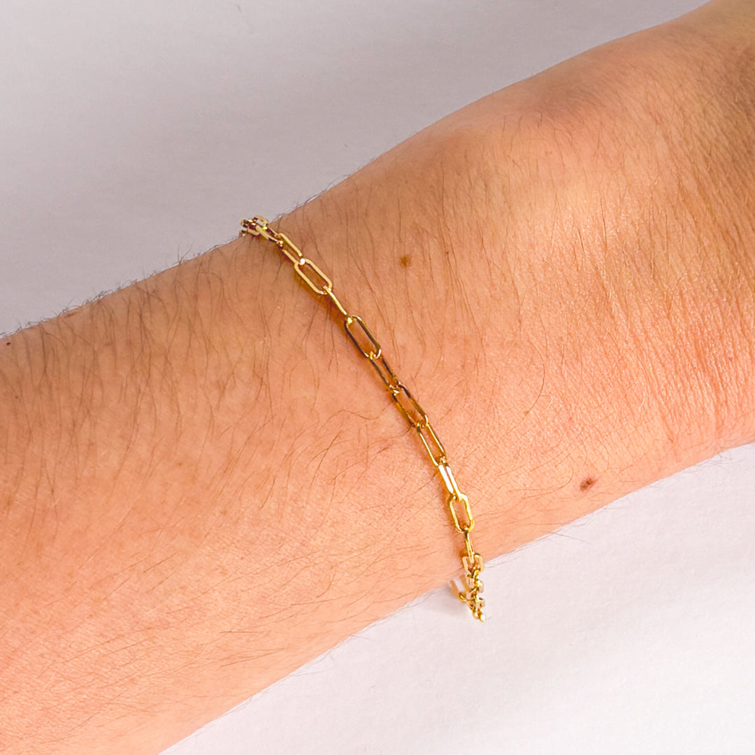 Gold chain bracelet on a wrist with a plain background