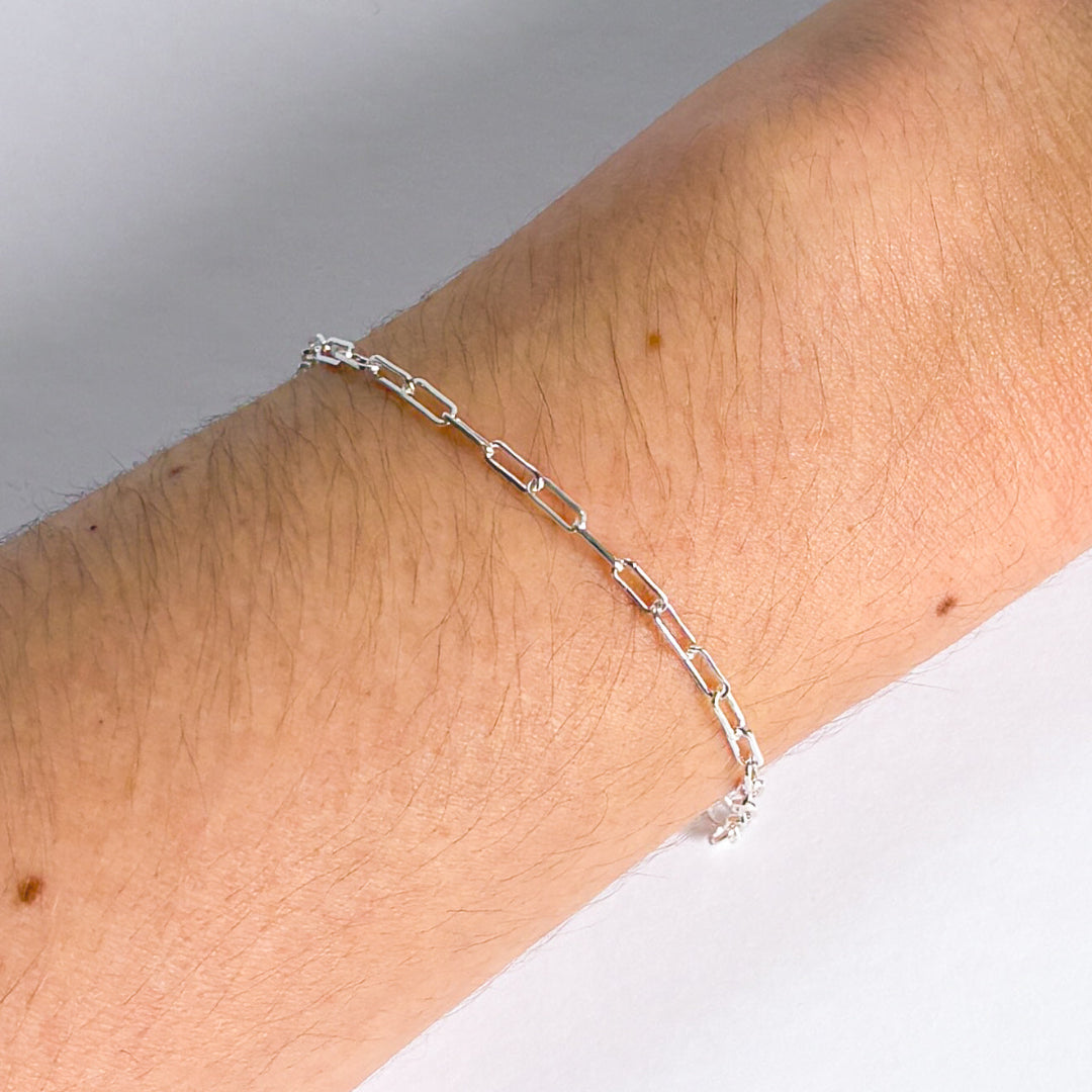 Silver chain bracelet on a wrist against a neutral background