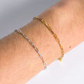 Two chain bracelets, one gold and one silver, on a wrist against a neutral background.