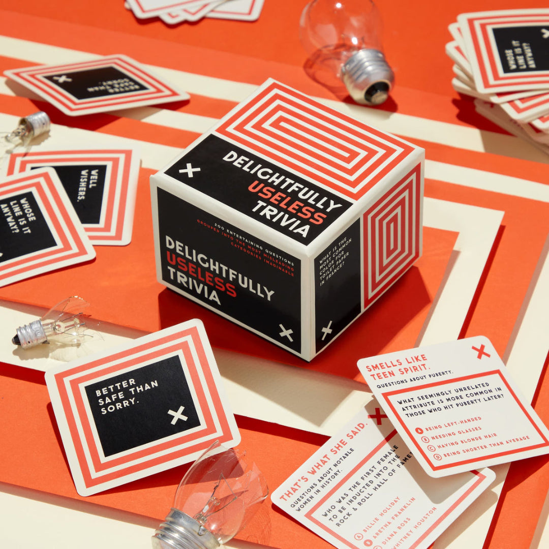 Delightfully Useless Trivia game box and cards on an orange surface with light bulbs.