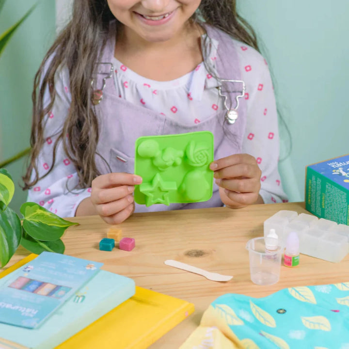 A cardboard box containing a Kiss Naturals Glycerin Soap Kit. The box is blue and white with the product name and a colorful illustration of penguins. It states that the kit is 100% natural, made in Canada, and suitable for ages 6 and up.