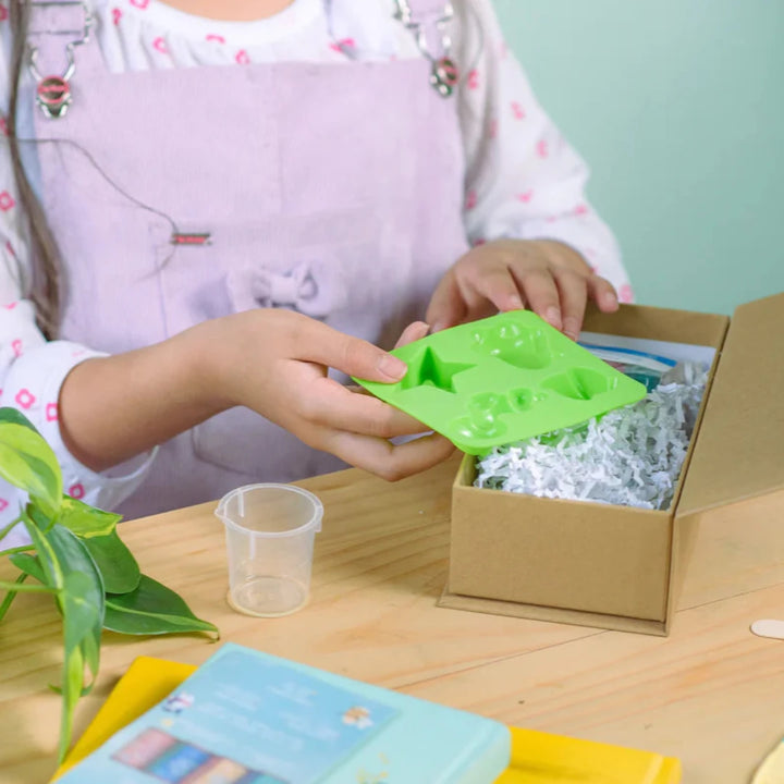 A cardboard box containing a Kiss Naturals Glycerin Soap Kit. The box is blue and white with the product name and a colorful illustration of penguins. It states that the kit is 100% natural, made in Canada, and suitable for ages 6 and up.