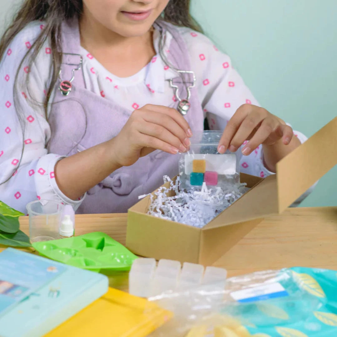 A cardboard box containing a Kiss Naturals Glycerin Soap Kit. The box is blue and white with the product name and a colorful illustration of penguins. It states that the kit is 100% natural, made in Canada, and suitable for ages 6 and up.