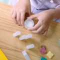 A cardboard box containing a Kiss Naturals Lip Balm Kit. The box is yellow and white with the product name and a colorful illustration of bees. It states that the kit is 100% natural, made in Canada, and suitable for ages 6 and up.