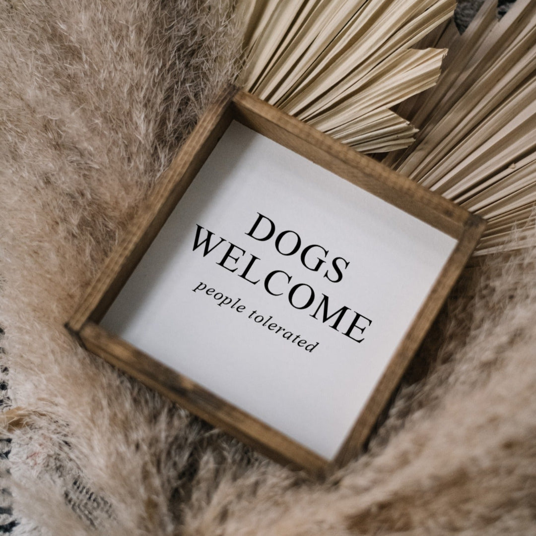 Decorative sign with 'DOGS WELCOME, people tolerated' text on a textured surface.