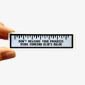 Sticker with a ruler design and motivational quote held by a hand on a white background