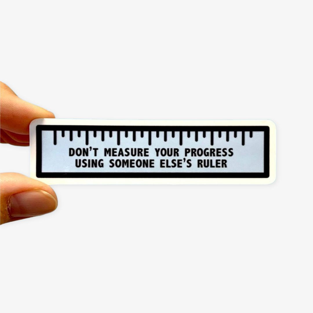Sticker with a ruler design and motivational quote held by a hand on a white background