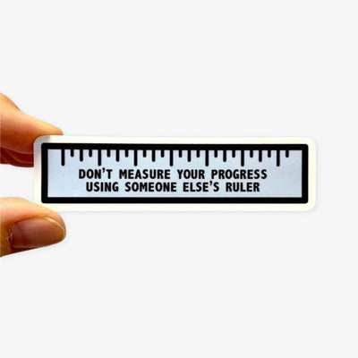 Sticker with a ruler design and motivational quote held by a hand on a white background