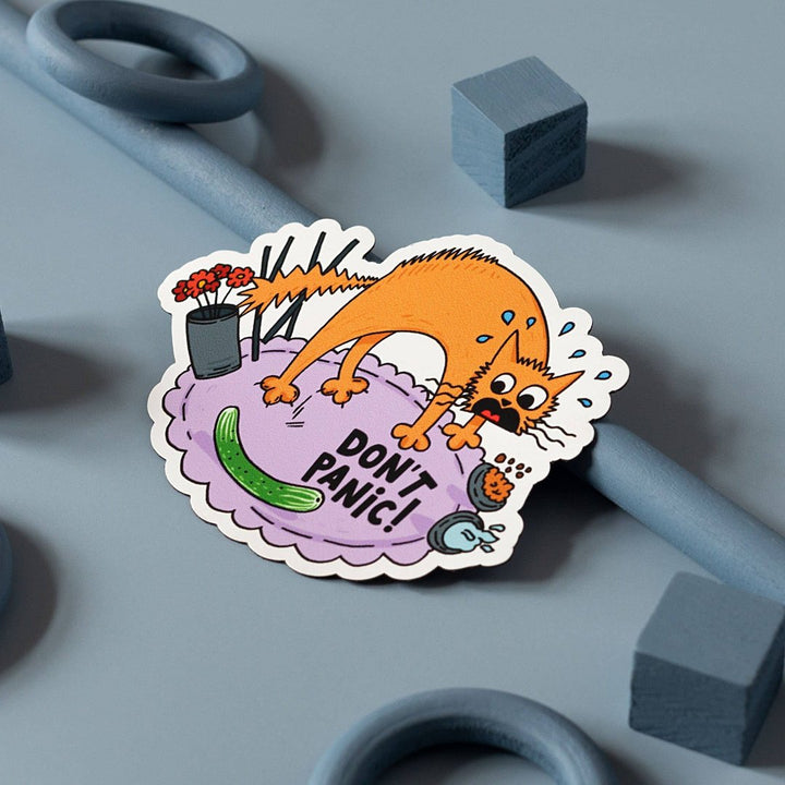 A cartoon illustration of a panicked orange cat surrounded by everyday objects like a vase, incense sticks, a cucumber, and a hairbrush. The text 