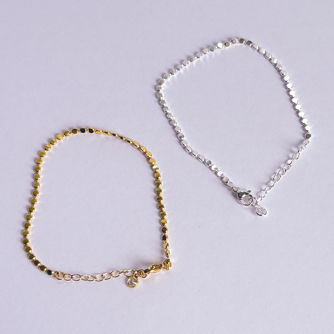 Gold and silver anklets on a light gray background