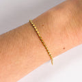 Gold bracelet on a wrist with a plain background