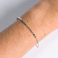 Close-up of a wrist wearing a silver bracelet with green beads on a neutral background
