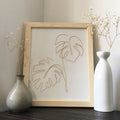 Framed artwork with leaf design on a wooden surface with decorative vases.
