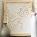 Two vases and a framed artwork with leaf design on a wooden surface.
