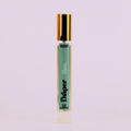 A small, cylindrical bottle of perfume with a gold cap. The bottle is transparent and filled with a light-colored liquid. The label on the bottle reads "Draper" in large, black letters. Below the brand name, it lists the fragrance notes: "Teak, Cardamom, Sandalwood."