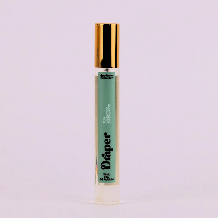 A small, cylindrical bottle of perfume with a gold cap. The bottle is transparent and filled with a light-colored liquid. The label on the bottle reads 