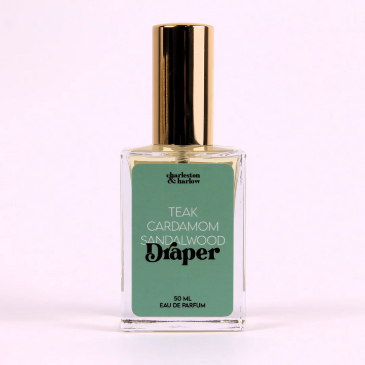 A small glass bottle of perfume with a gold cap. The bottle is transparent and filled with a light-colored liquid. The label on the bottle reads 