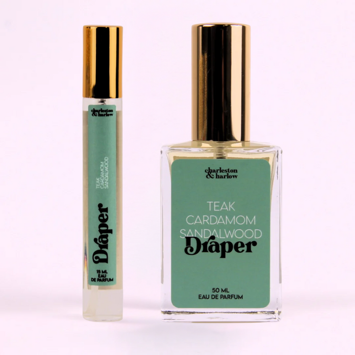 A small, cylindrical bottle of perfume with a gold cap. The bottle is transparent and filled with a light-colored liquid. The label on the bottle reads 