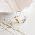 Two gold and silver duck-shaped pendants on necklaces with a soft background.